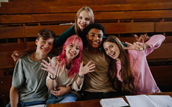 A diverse group of college students smiling and posing in a university lecture hall, displaying camaraderie and happiness. They showcase teamwork, education, and friendship in an academic environment.